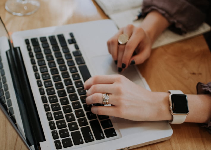 Hände mit Ringen und einer Uhr am Laptop